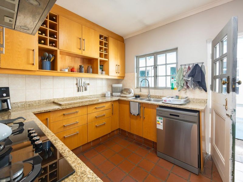 Functional kitchen featuring warm-toned wooden cabinetry, granite countertops, a gas hob with extractor, and durable tiled flooring with direct outdoor access.