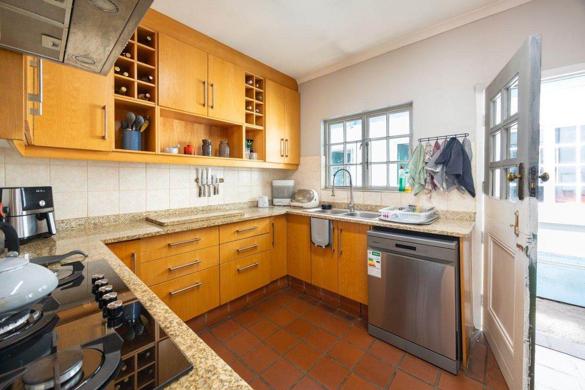 Functional kitchen featuring warm-toned wooden cabinetry, granite countertops, a gas hob with extractor, and durable tiled flooring with direct outdoor access.