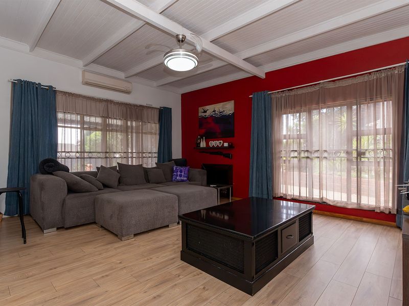 A living room featuring exposed beam ceilings, a ceiling fan, split system air conditioning, and laminate flooring with large windows and security gates.
