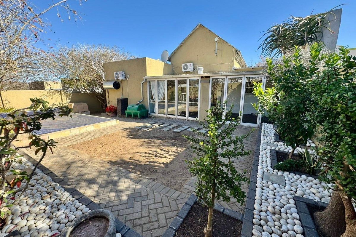Rear exterior view featuring a paved patio area, landscaped garden with pebble borders, and large bi-fold doors leading into the home.