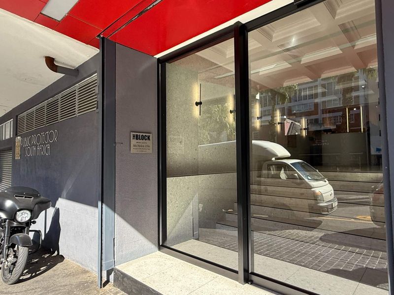 Front entrance of the office building featuring large glass sliding doors and modern signage under a covered walkway.