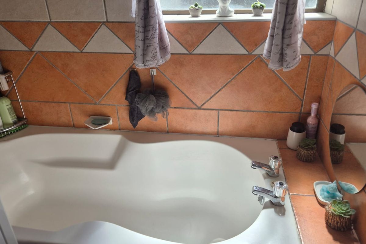 A bathroom featuring a built-in bathtub with chrome fixtures and decorative orange and white ceramic wall tiling.
