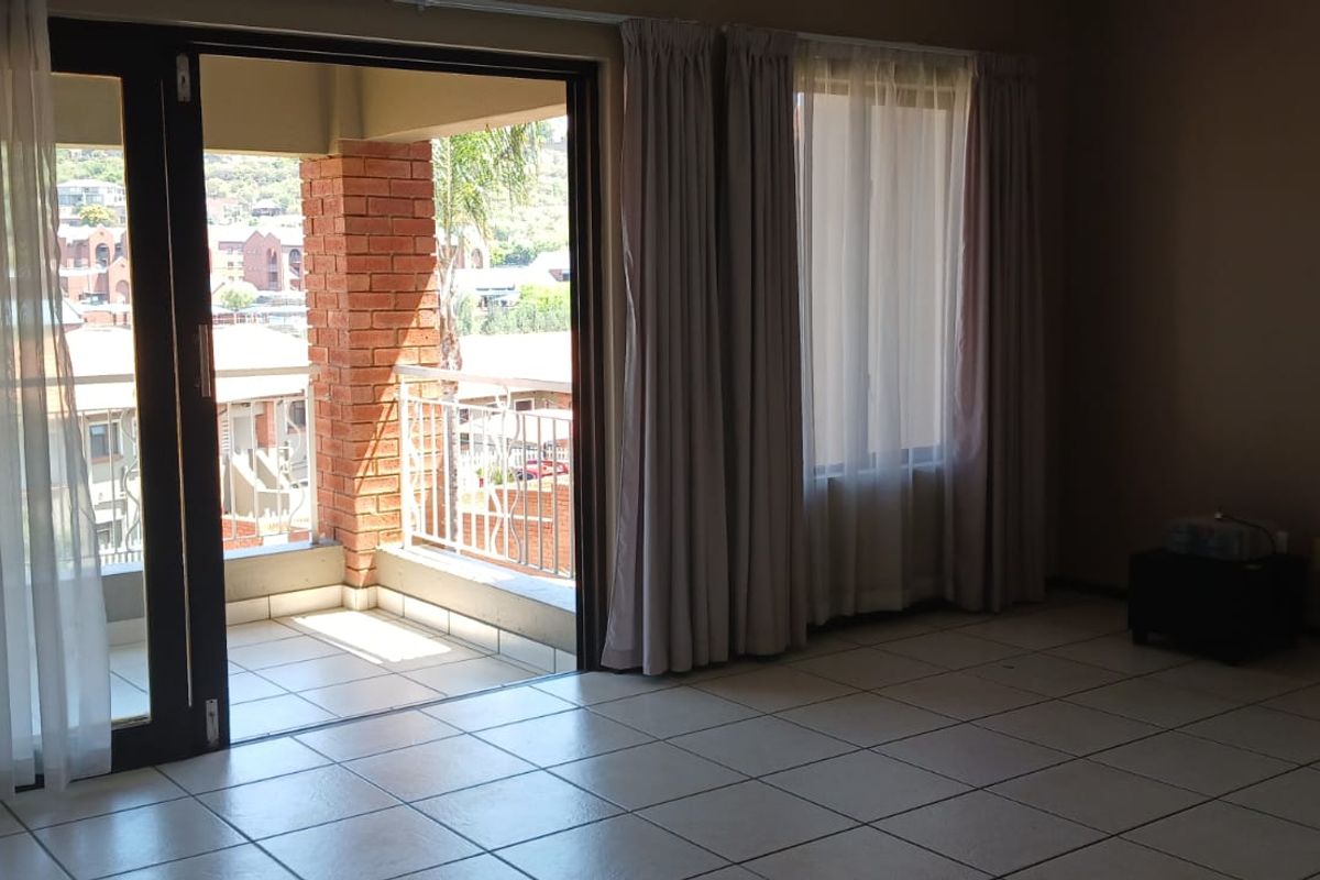 An empty living room with tiled flooring and large sliding glass doors leading out to a private balcony with brick and metal detailing.