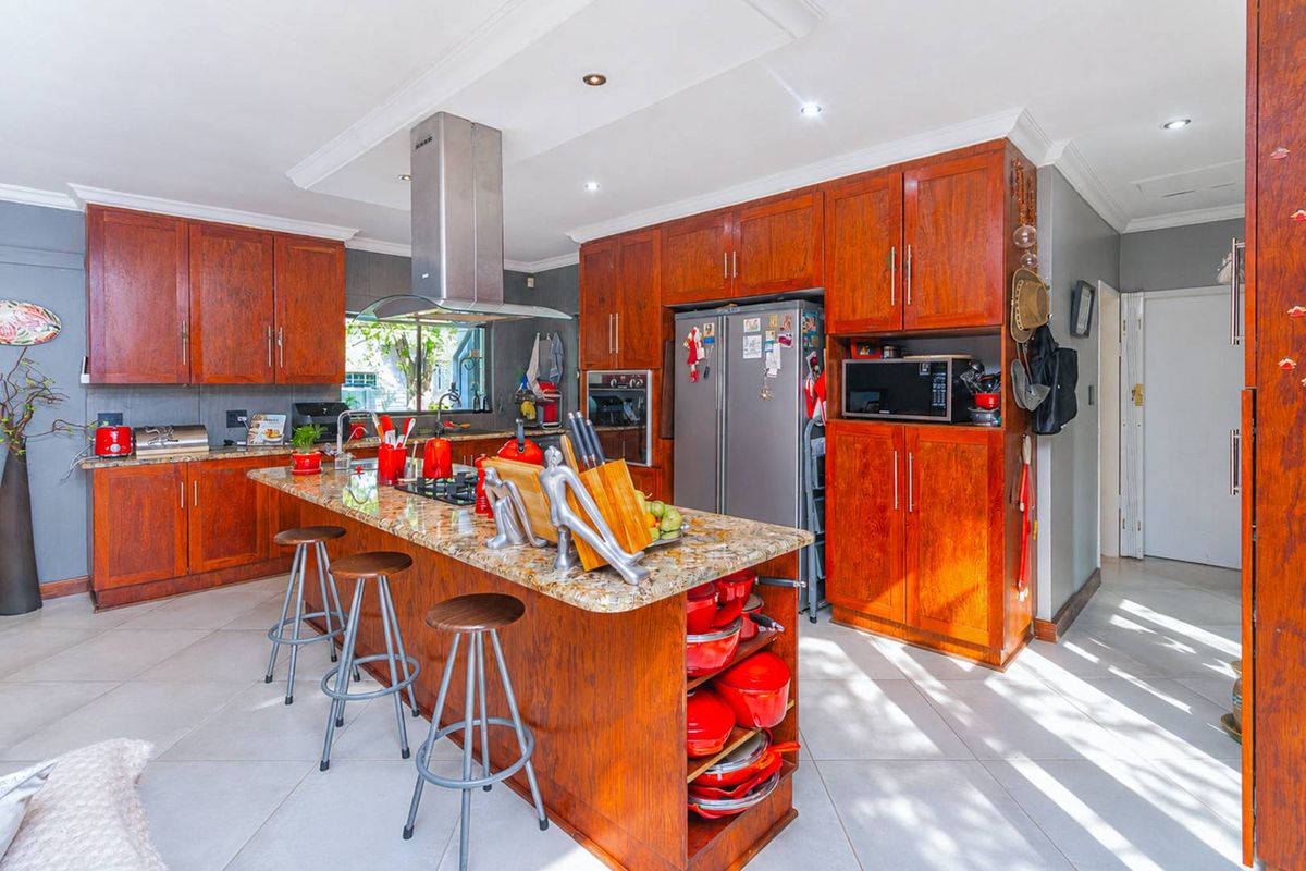 Spacious kitchen featuring warm-toned wooden cabinetry, granite countertops, a central island with breakfast bar seating, and a stainless steel extractor fan.