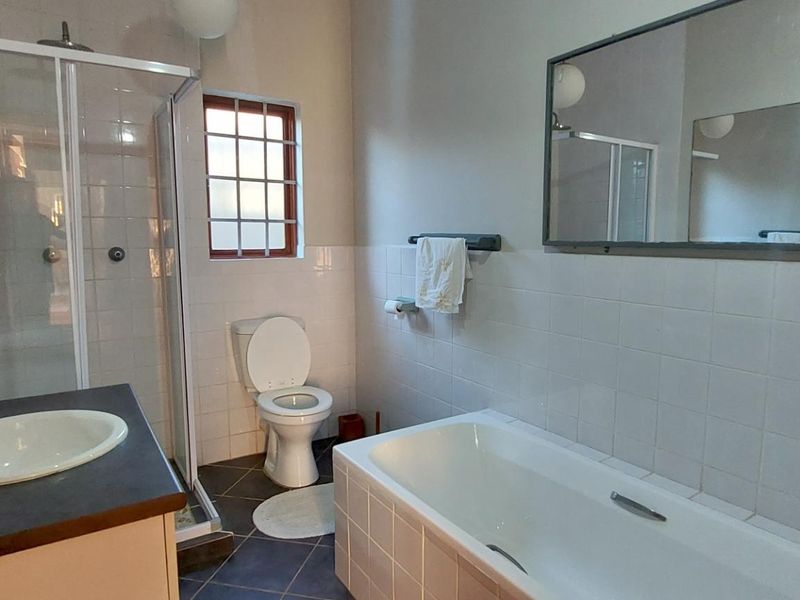 A functional bathroom featuring a shower enclosure, bathtub, built-in vanity with basin, and toilet, finished with white wall tiles and dark floor tiles.
