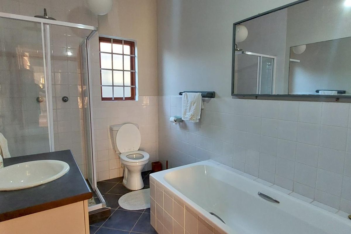 A functional bathroom featuring a shower enclosure, bathtub, built-in vanity with basin, and toilet, finished with white wall tiles and dark floor tiles.