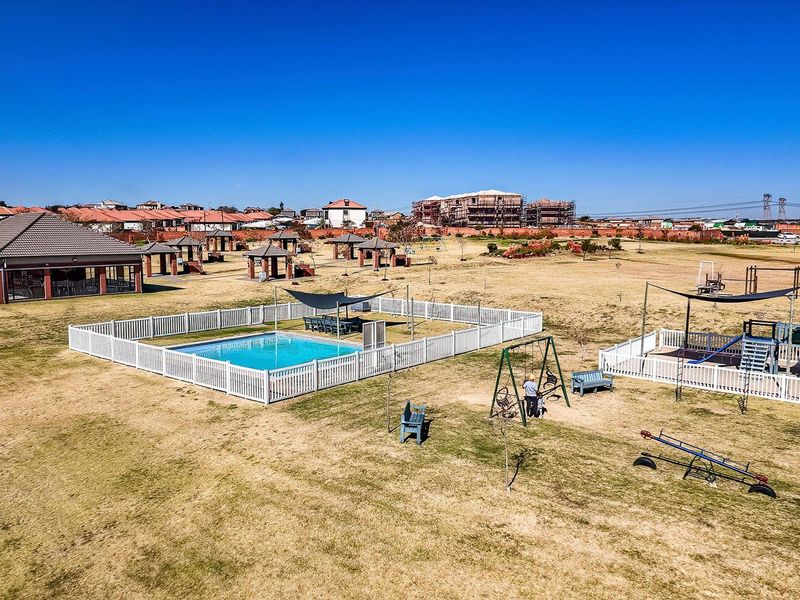 Aerial view of a residential estate featuring a communal swimming pool, clubhouse, and playground facilities set within expansive landscaped grounds.