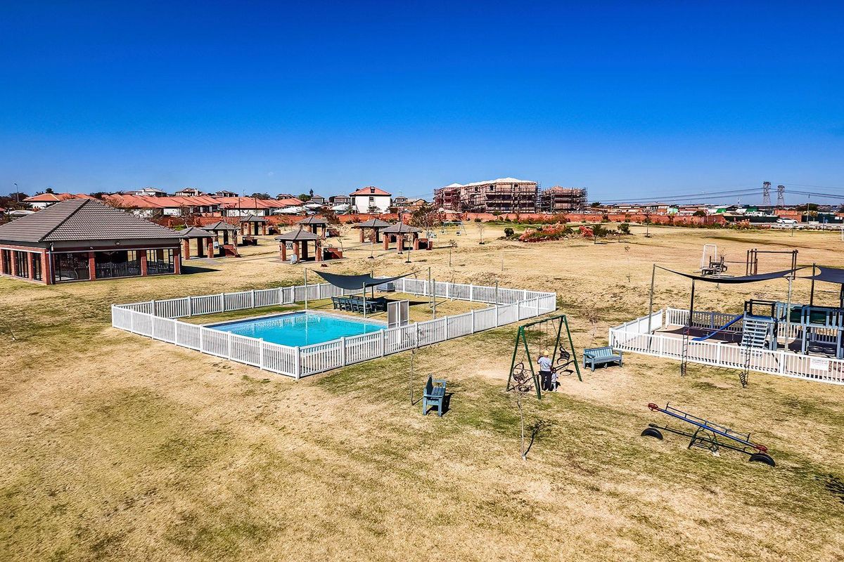 Aerial view of a residential estate featuring a communal swimming pool, clubhouse, and playground facilities set within expansive landscaped grounds.