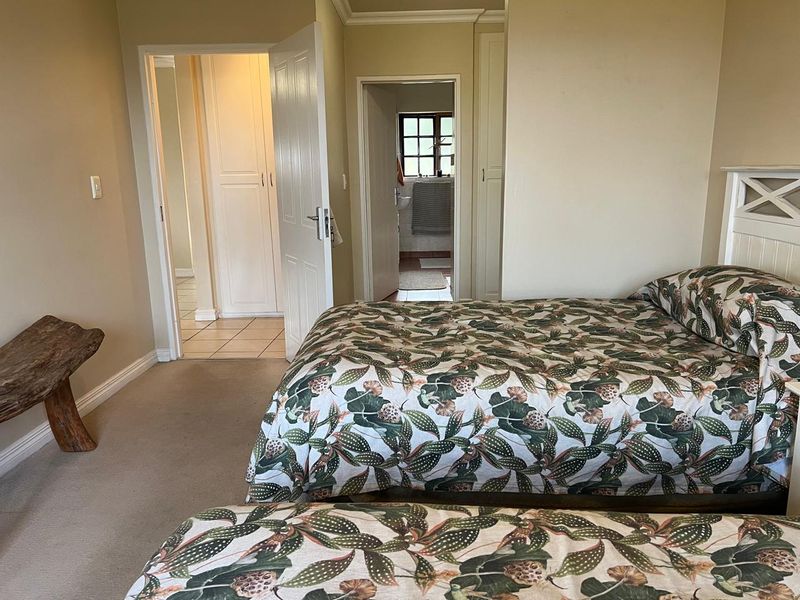 A bedroom featuring built-in cupboards, neutral wall tones, and carpeted flooring, with an adjoining en-suite bathroom visible through the doorway.