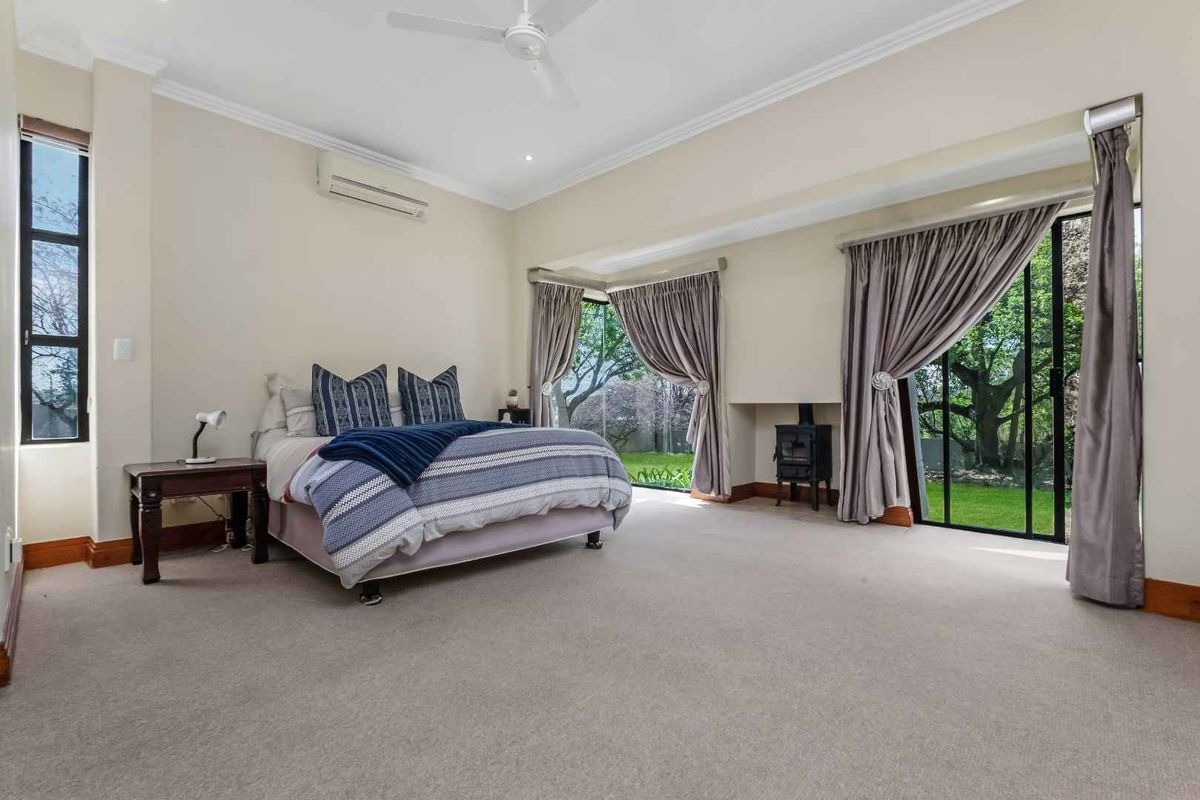 Spacious bedroom featuring neutral carpeting, a ceiling fan, split system air conditioning, a cozy wood-burning stove, and direct access to the garden via sliding doors.