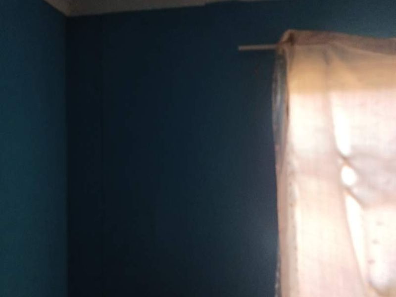 A bedroom corner featuring blue painted walls and ceiling cornice, currently showing poor lighting and low image quality.