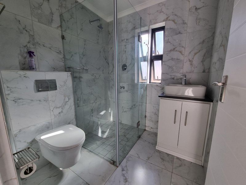 Modern bathroom featuring marble-look tiling, a glass-enclosed shower, a wall-mounted toilet, and a vanity unit with a vessel sink.