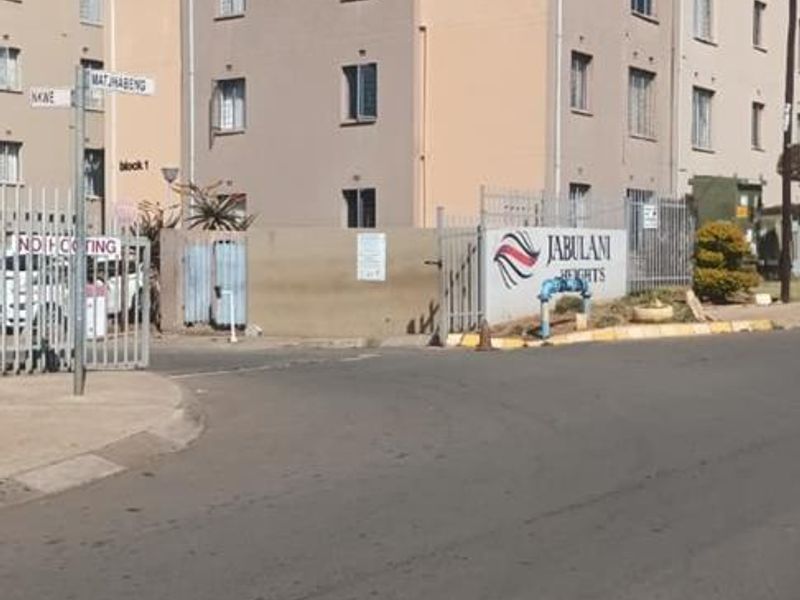 Street view of Jabulani Heights townhouse complex featuring multi-story residential buildings, perimeter fencing, and gated access.