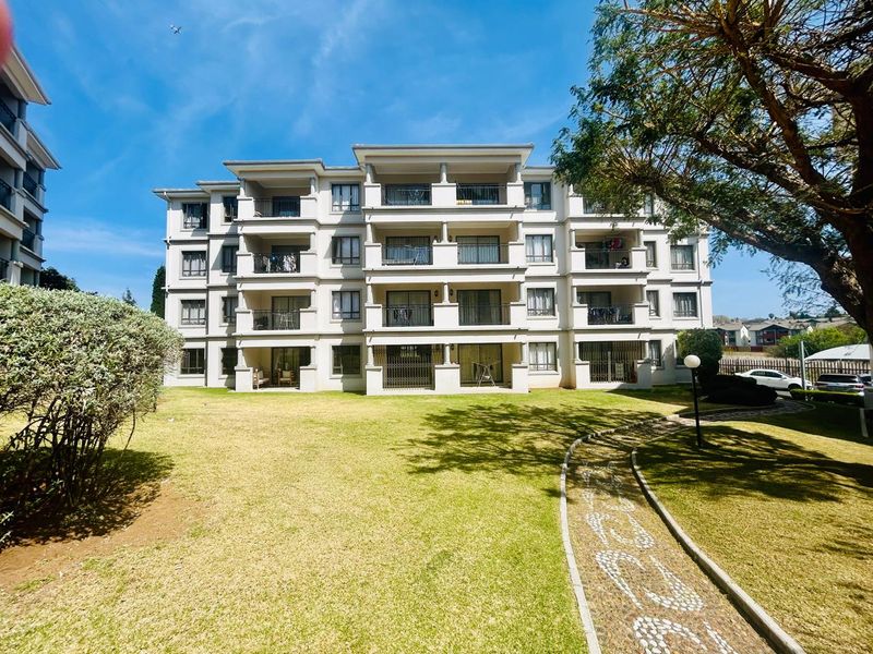 A view of the rear apartment building facade featuring multiple balconies, sliding glass doors, and a well-maintained communal lawn and paved walkway.