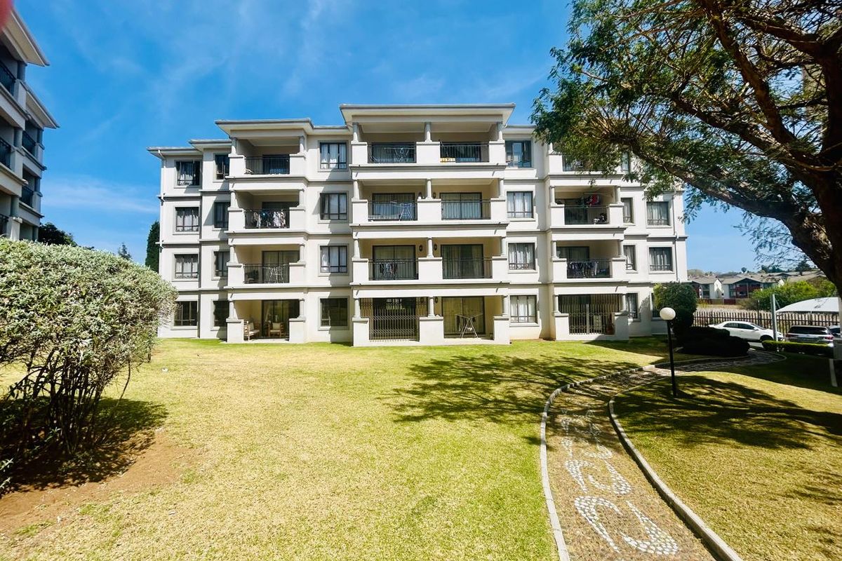 A view of the rear apartment building facade featuring multiple balconies, sliding glass doors, and a well-maintained communal lawn and paved walkway.
