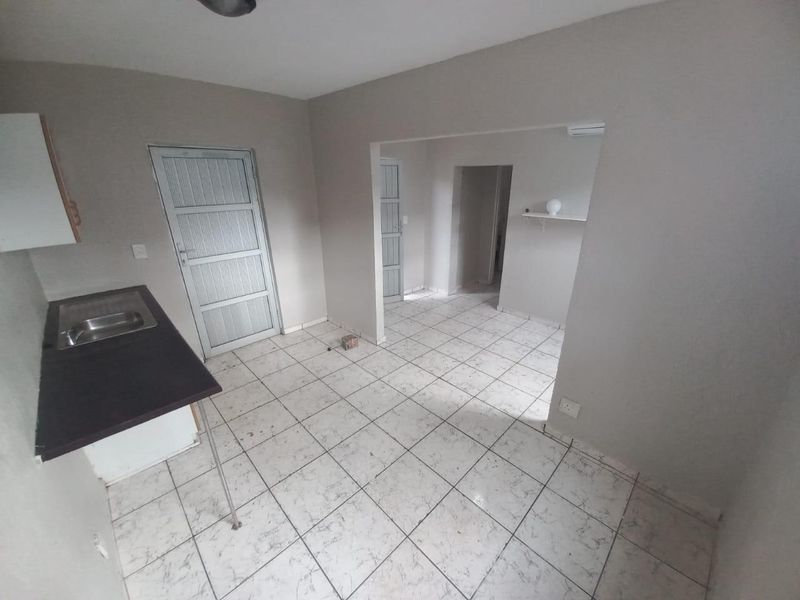 An empty kitchen area featuring tiled flooring, a basic sink with a laminate countertop, and direct access to adjacent rooms.