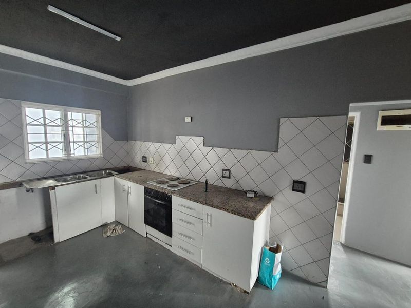 A functional kitchen featuring granite countertops, built-in oven, electric hob, and double sink, with potential for cosmetic updates to the tiling and paintwork.