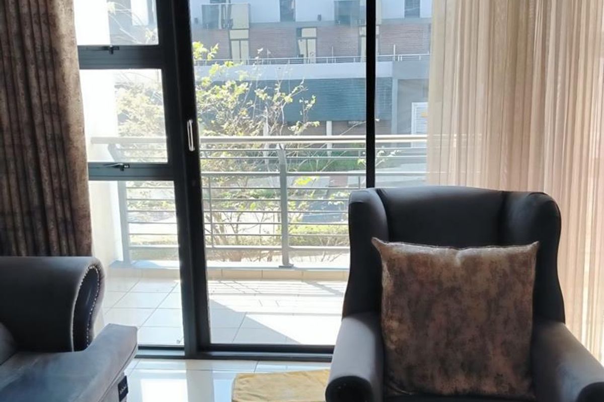 A bright living room featuring large sliding glass doors that open onto a private balcony, with polished tiled flooring throughout.
