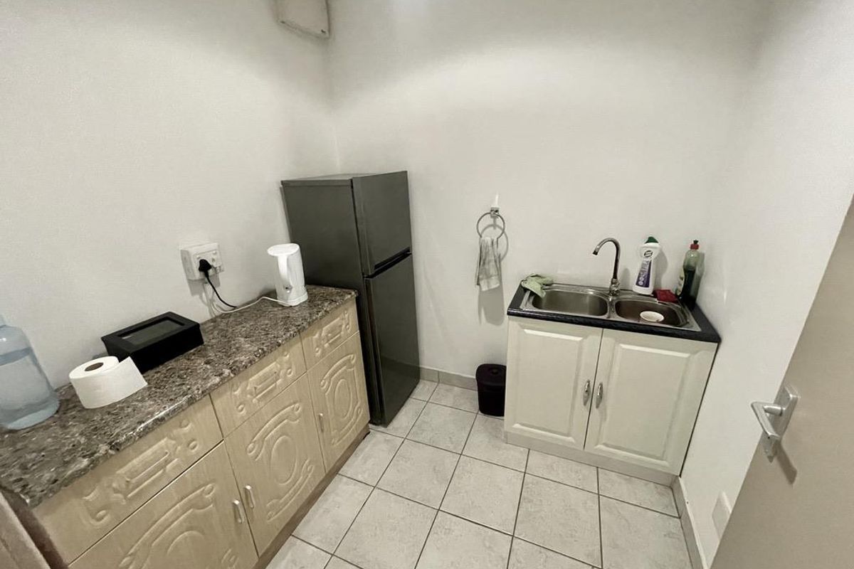 A compact kitchenette area featuring built-in cabinetry, a double-basin sink, granite-look countertops, and tiled flooring, suitable for office or utility use.