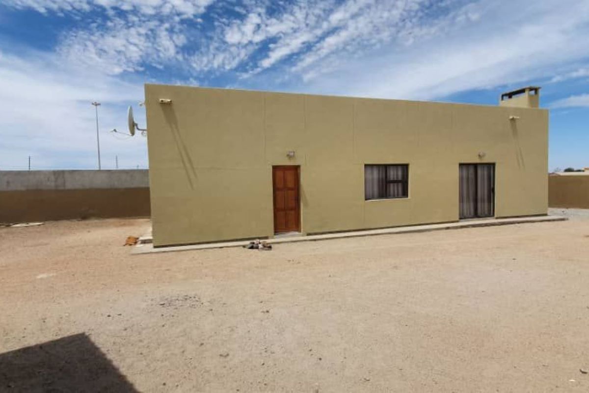 Rear view of the property featuring a plain exterior facade, a single door, a window, and a large, unpaved yard area.