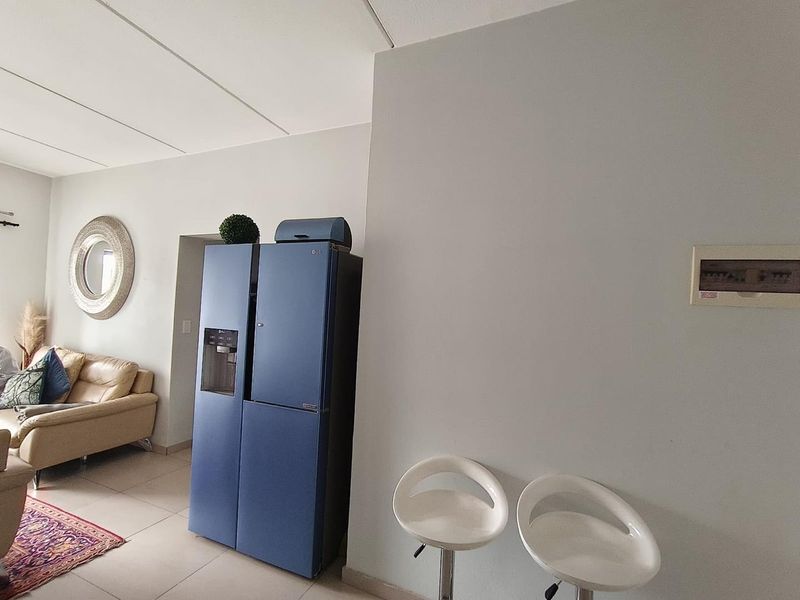 An open-plan living area featuring tiled flooring and a wall-mounted electrical distribution board, connecting to the adjacent lounge space.