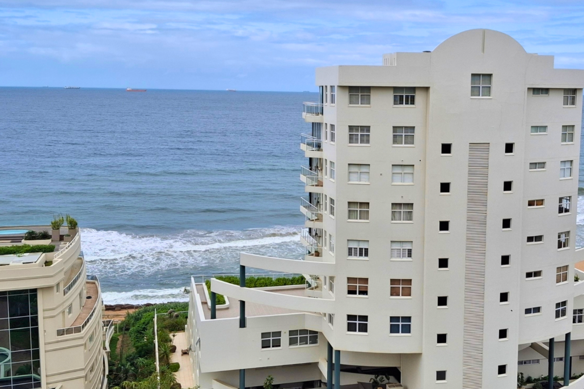 An elevated aerial view of a coastal apartment building featuring balconies and direct ocean views.