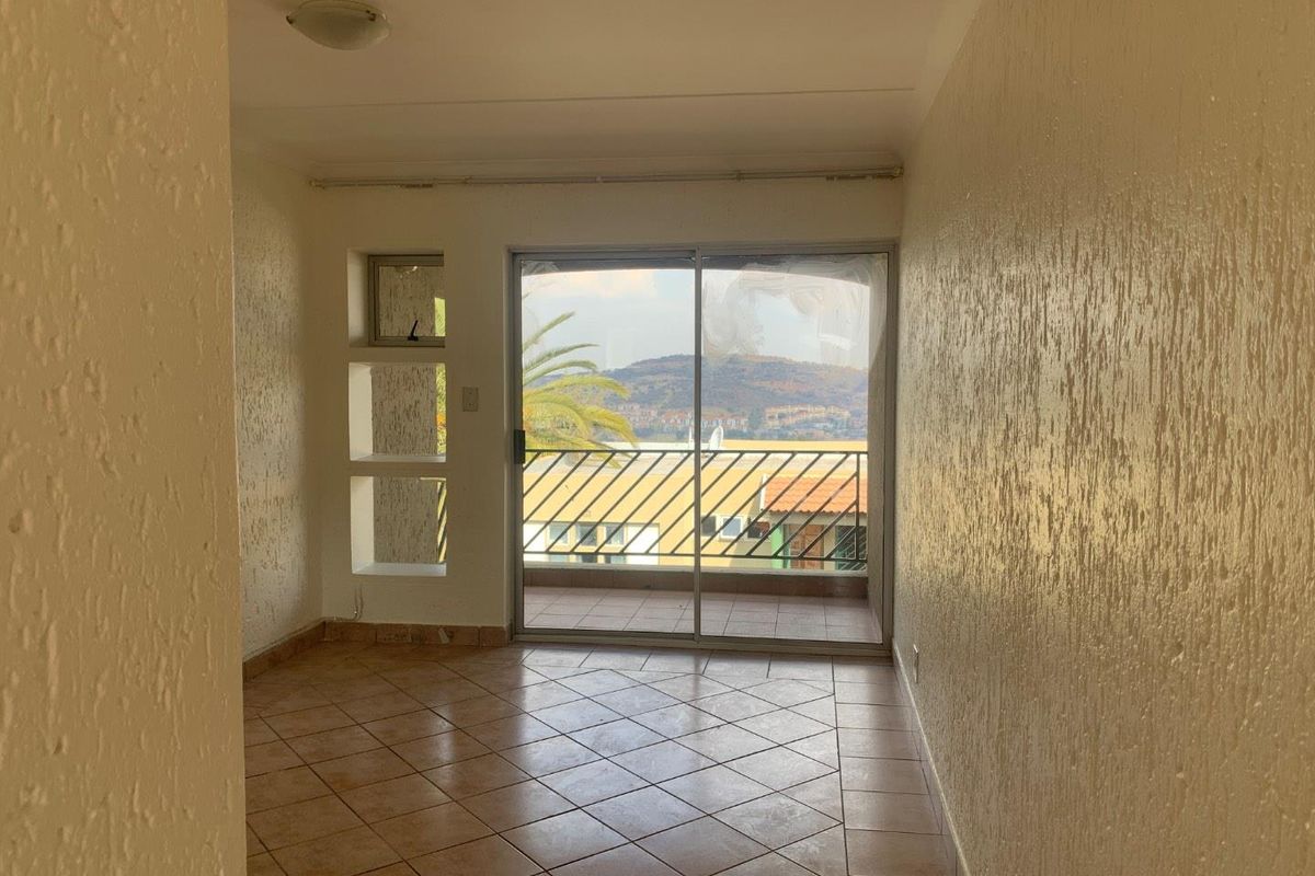 An empty living area featuring tiled flooring, textured walls, and a sliding glass door leading to a balcony with scenic views.