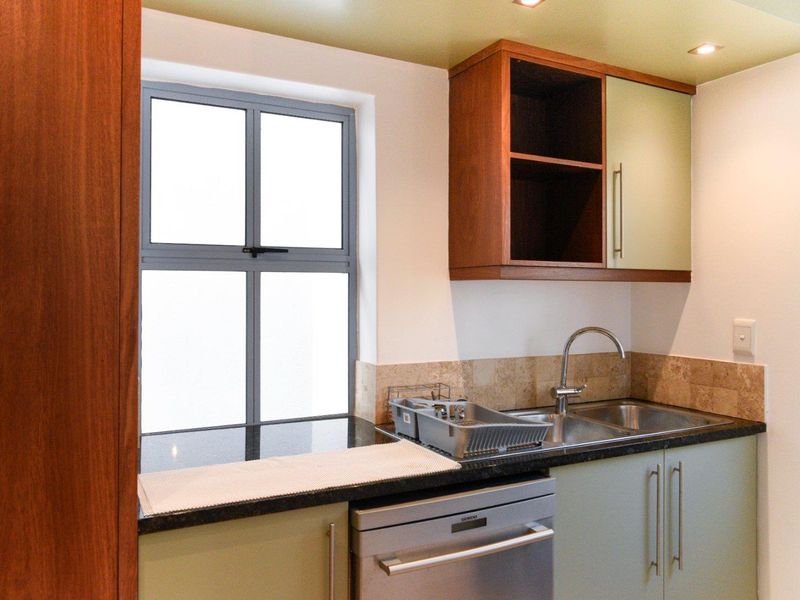 A functional kitchen area featuring built-in cabinetry, stone countertops, a stainless steel sink with mixer tap, and integrated dishwasher.