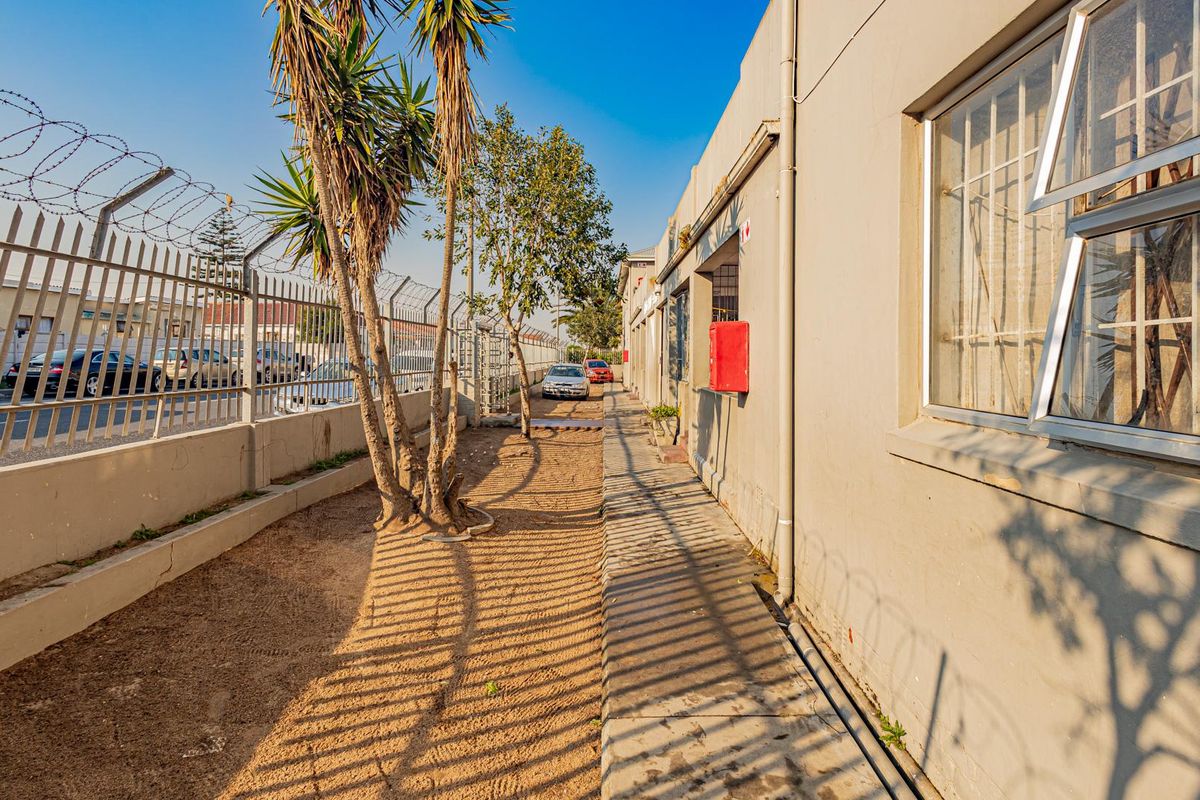 Exterior side passage of the apartment building featuring a concrete walkway, security fencing with razor wire, and external wall access.