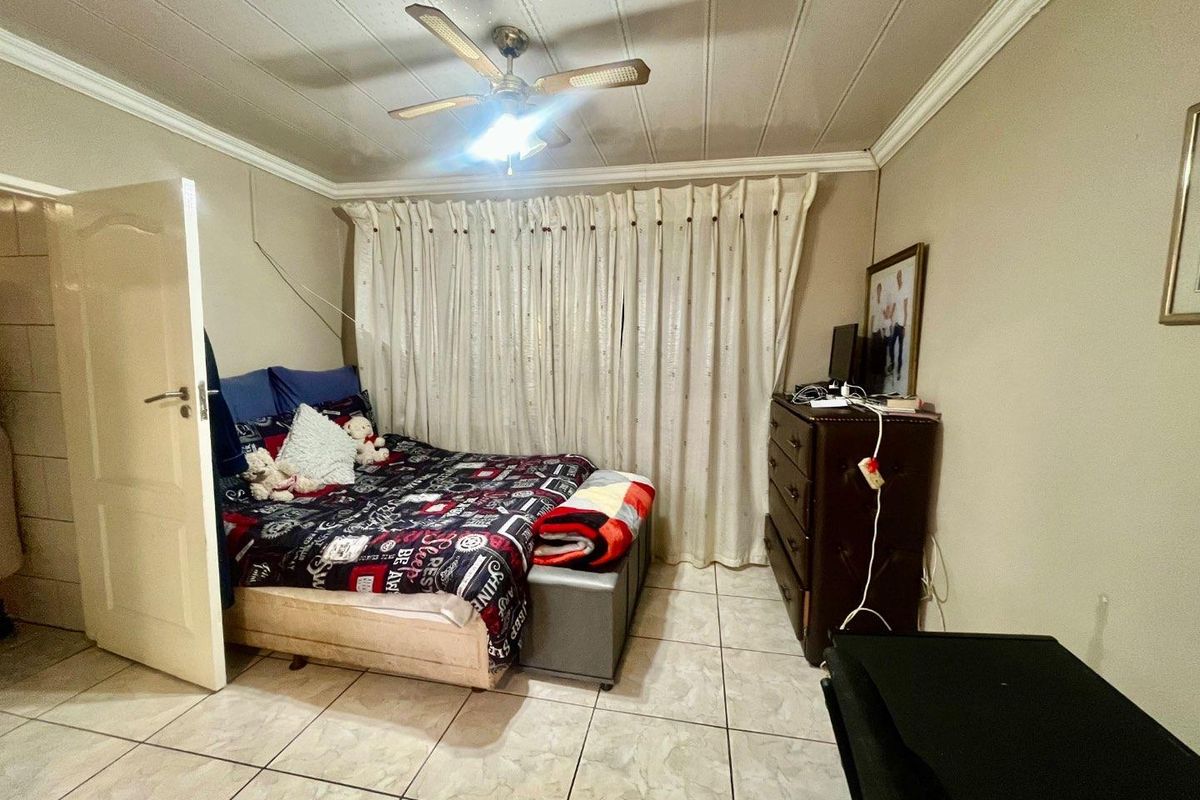 A bedroom featuring tiled flooring, a ceiling fan, and crown molding, providing a functional living space.