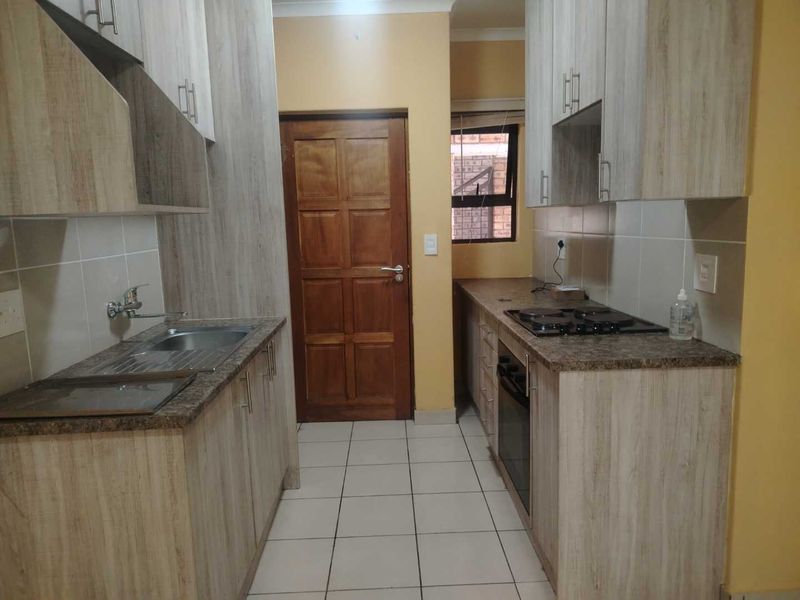 A functional galley-style kitchen featuring light wood-grain cabinetry, granite countertops, built-in oven and hob, and tiled flooring.