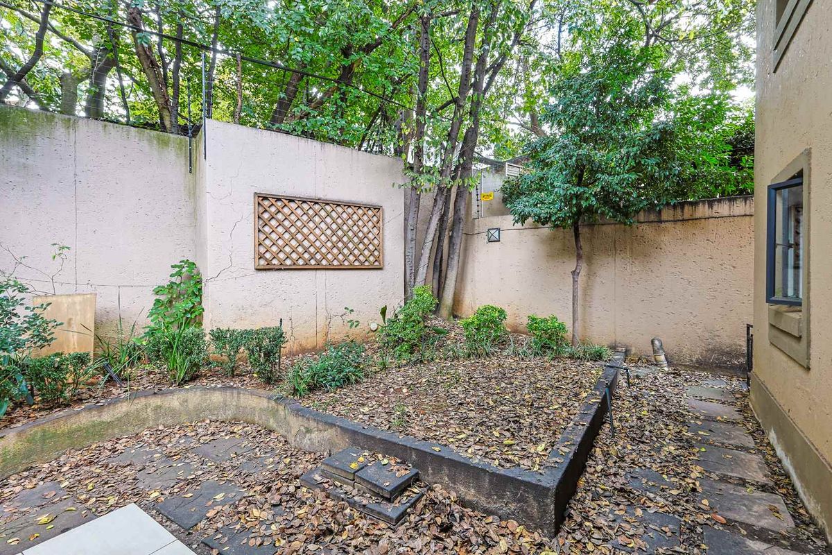 A private rear garden area featuring a raised planter bed, paved pathways, and high boundary walls, requiring maintenance and landscaping.