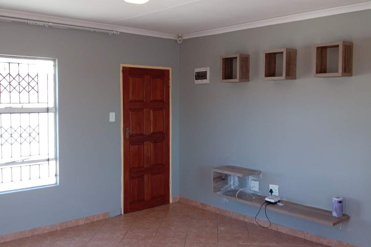 A living room featuring tiled flooring, a wooden door, a security-barred window, and built-in wall-mounted shelving units.