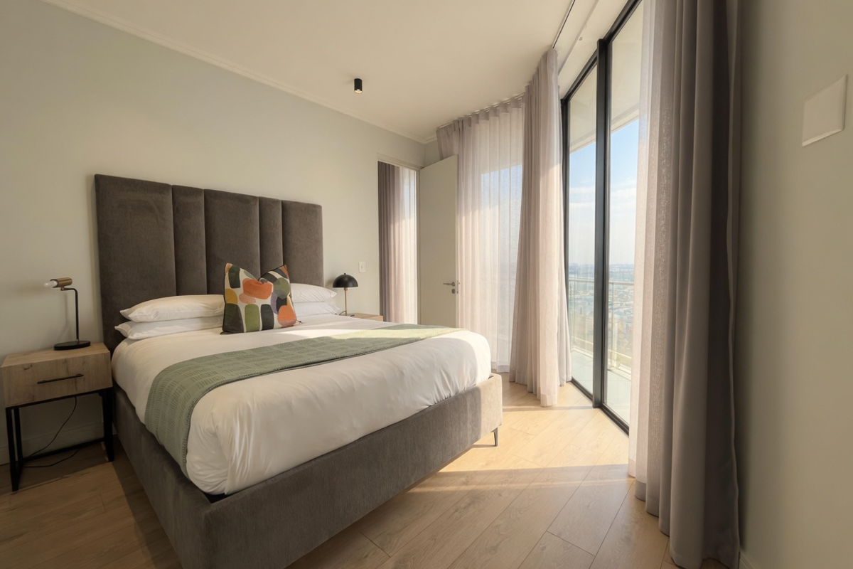 Modern bedroom featuring floor-to-ceiling windows with natural light, laminate flooring, and recessed ceiling lighting, offering a bright and contemporary living space.