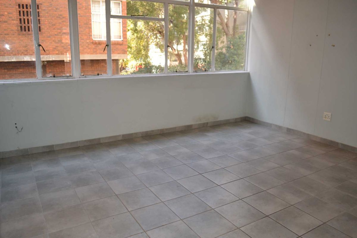 An empty, sunlit room featuring large windows, tiled flooring, and neutral walls, offering a blank canvas for renovation or interior design.