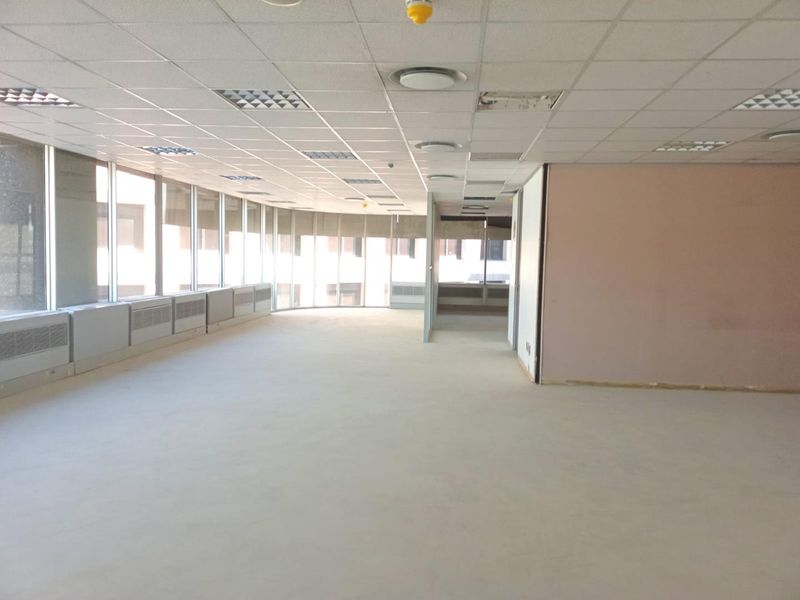 An expansive, empty open-plan office space featuring large floor-to-ceiling windows, a suspended ceiling with recessed lighting, and neutral flooring.