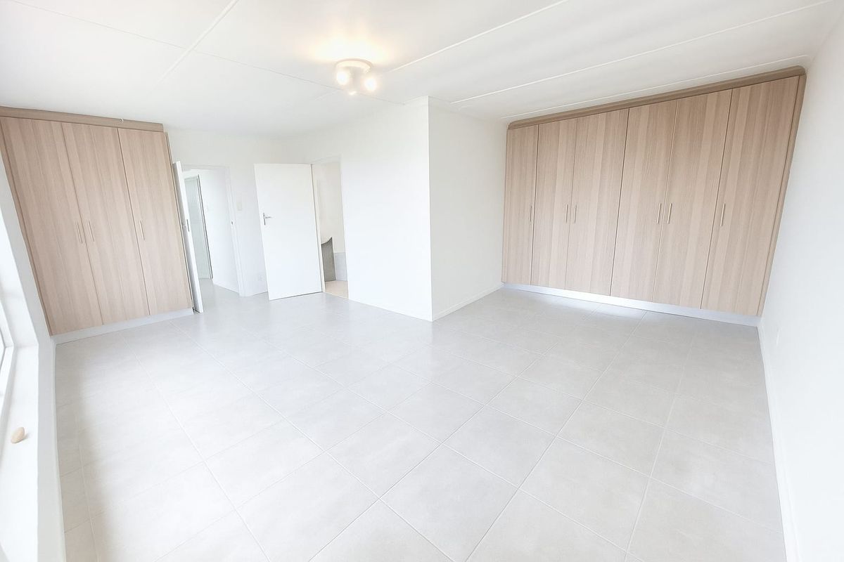 A bright, spacious bedroom featuring neutral floor tiles and extensive built-in wooden cabinetry for ample storage.