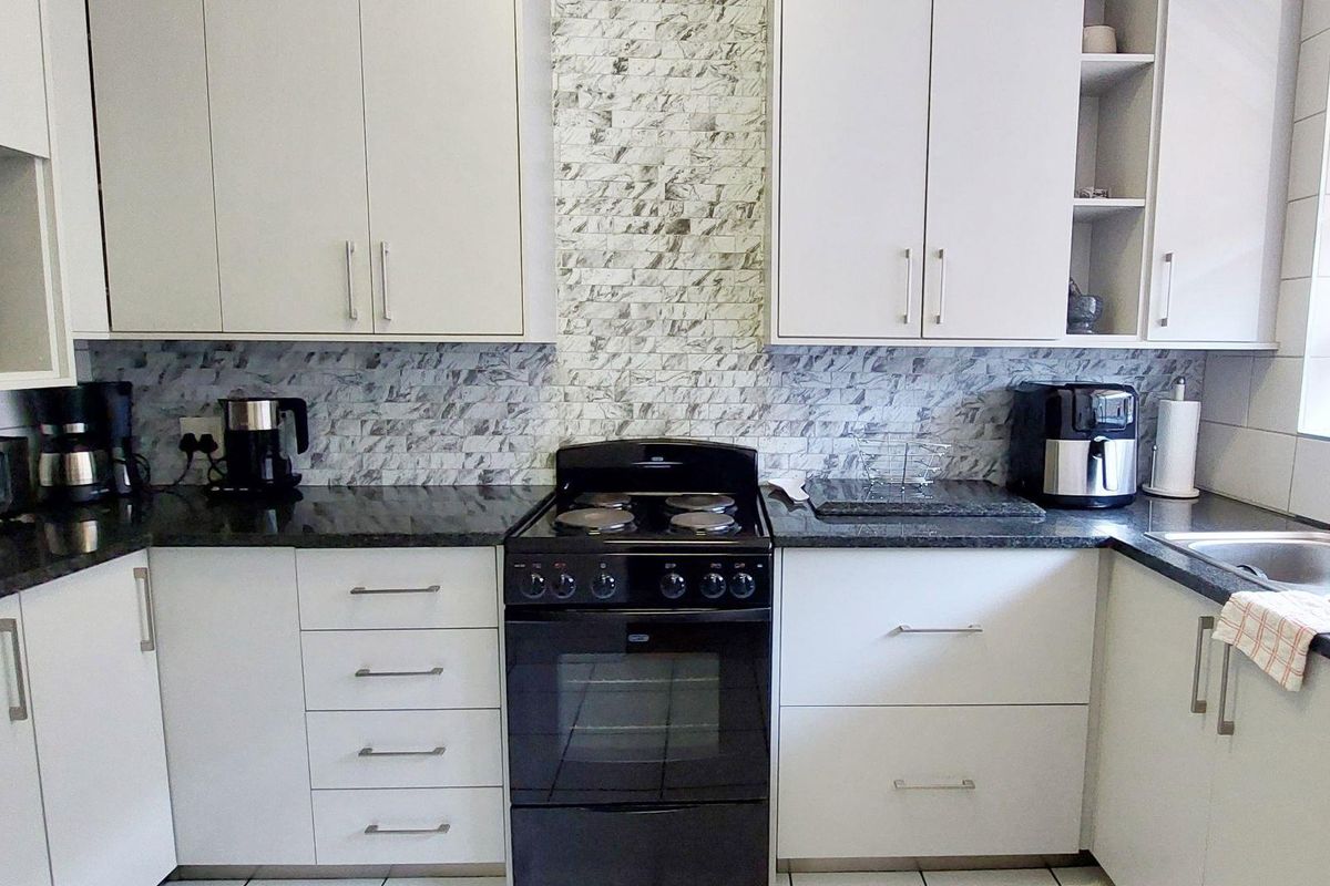 A functional kitchen featuring white cabinetry, dark granite countertops, a marble-look mosaic backsplash, and a freestanding electric stove.