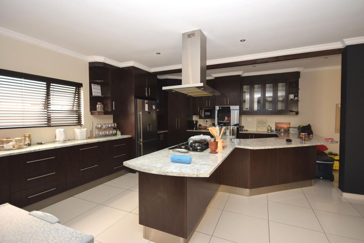 Modern kitchen featuring dark wood cabinetry, stone countertops, a central island with a gas hob, and integrated stainless steel appliances.