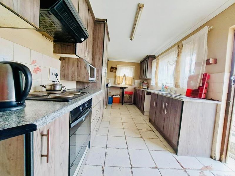 A functional galley-style kitchen featuring laminate cabinetry, built-in oven, electric hob, and tiled flooring, offering potential for modernization.