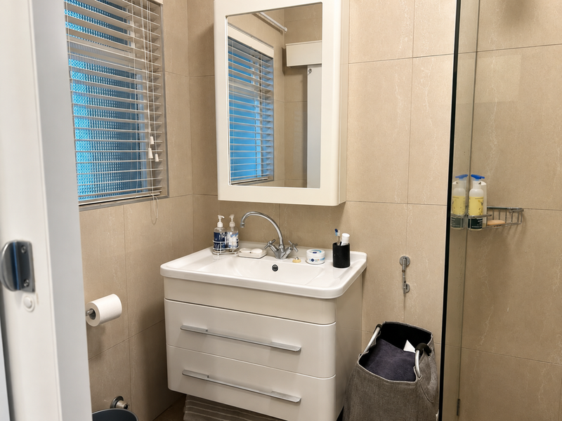 A modern bathroom featuring a wall-mounted vanity with basin, integrated medicine cabinet, and a glass-enclosed shower with neutral wall tiling.