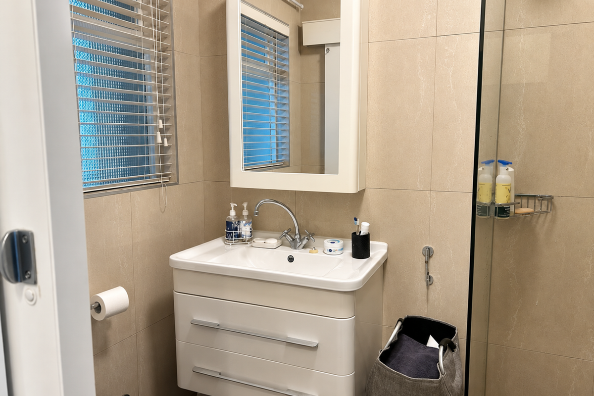 A modern bathroom featuring a wall-mounted vanity with basin, integrated medicine cabinet, and a glass-enclosed shower with neutral wall tiling.