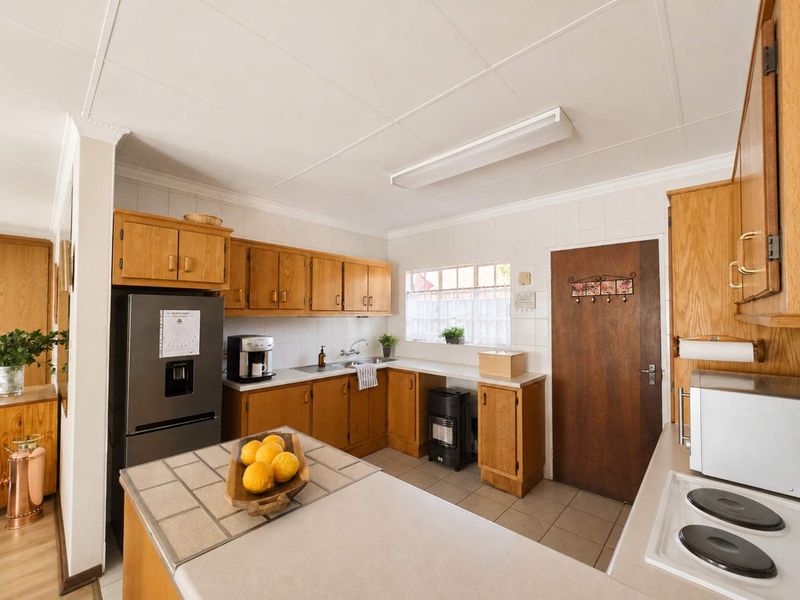 A functional kitchen featuring traditional wooden cabinetry, tiled countertops, and a tiled splashback, offering a classic layout with ample storage space.