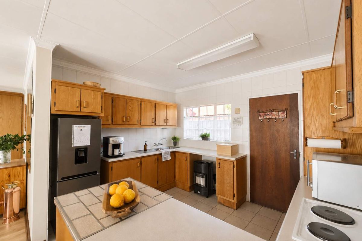 A functional kitchen featuring traditional wooden cabinetry, tiled countertops, and a tiled splashback, offering a classic layout with ample storage space.