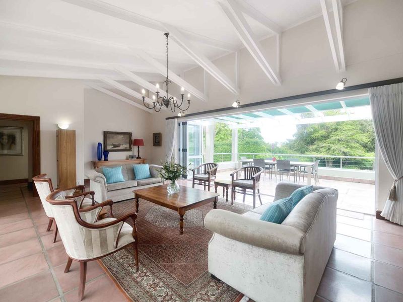 Spacious living room featuring vaulted ceilings with exposed rafters, terracotta flooring, and large folding glass doors opening onto a covered patio.