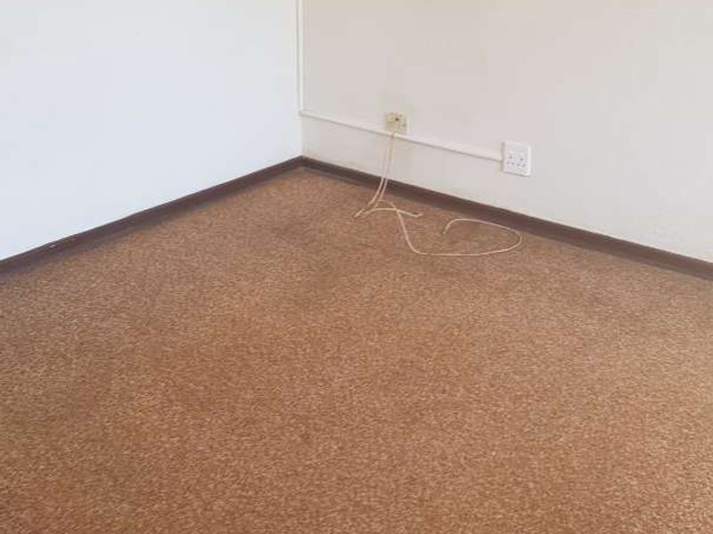 An empty bedroom featuring worn brown carpeting and surface-mounted electrical wiring along the wall.