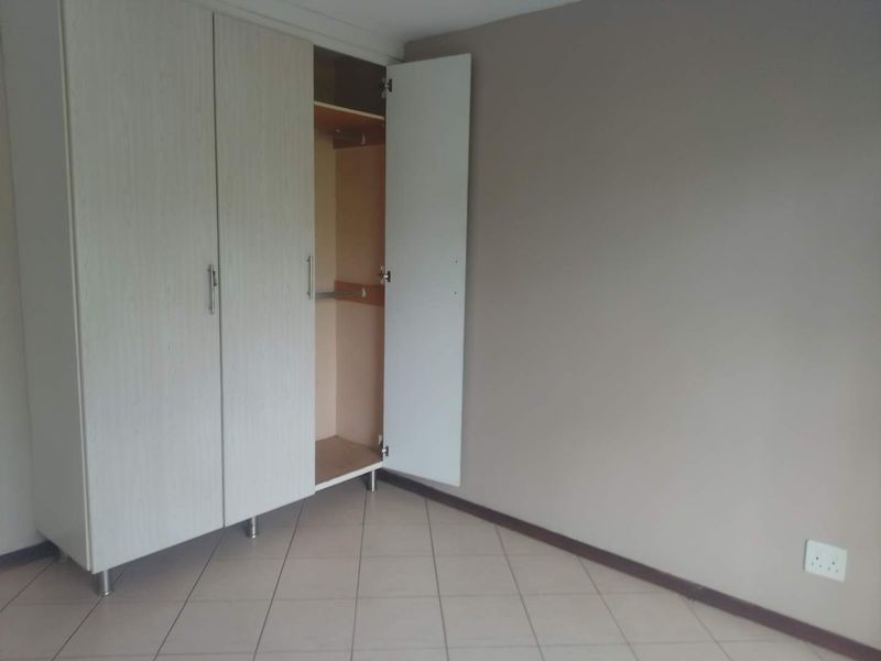 A clean, empty bedroom featuring neutral wall tones, tiled flooring, and a functional built-in wardrobe with ample storage space.
