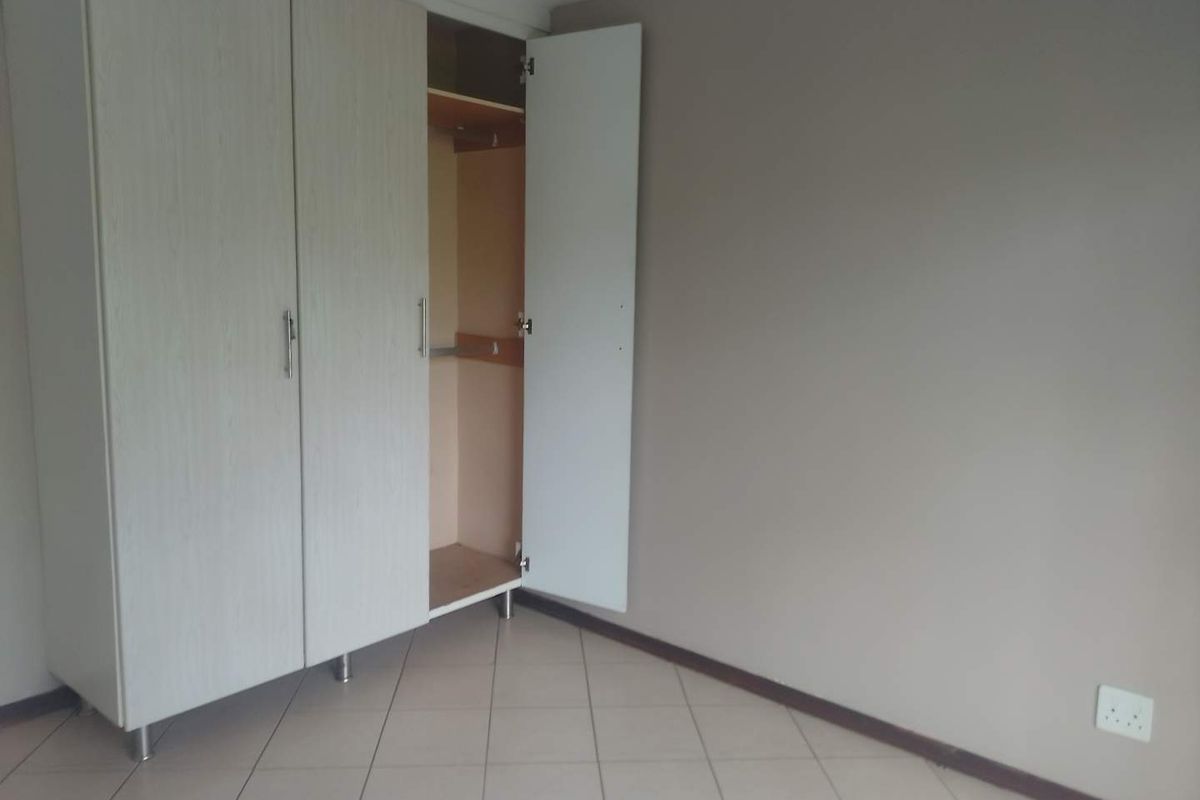 A clean, empty bedroom featuring neutral wall tones, tiled flooring, and a functional built-in wardrobe with ample storage space.