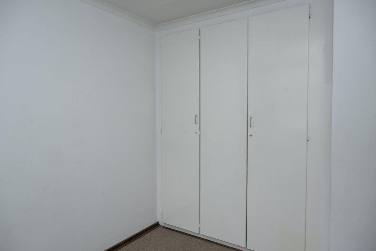 A simple bedroom featuring built-in storage cupboards with white doors and neutral carpeting.