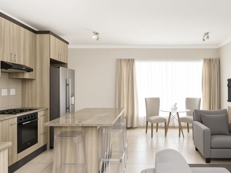 Modern open-plan living area featuring a well-appointed kitchen with stone countertops, built-in appliances, and a functional island, seamlessly flowing into the dining and lounge space.